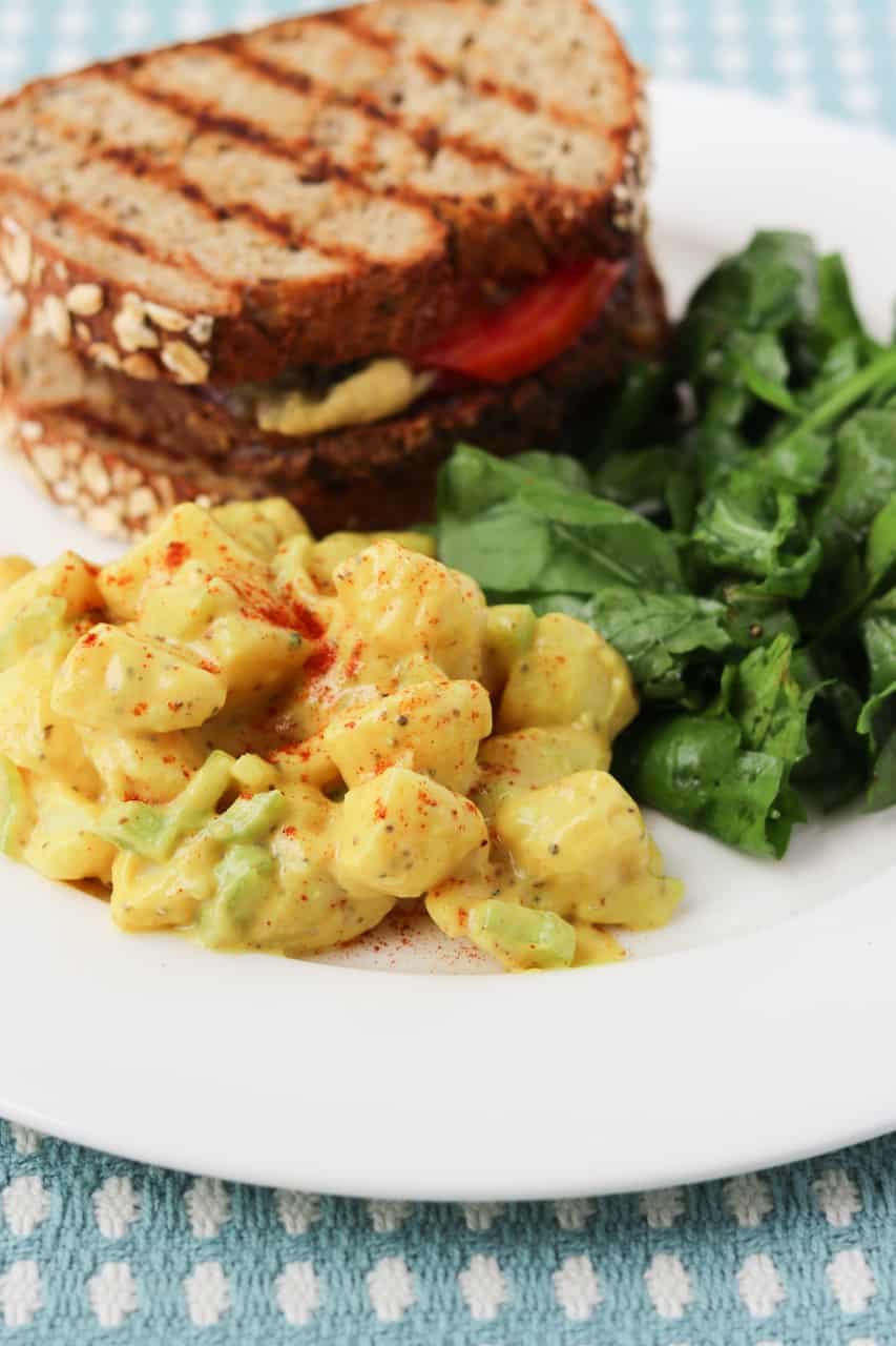 Grilled veggie burger on a plate with creamy potato salad and fresh greens