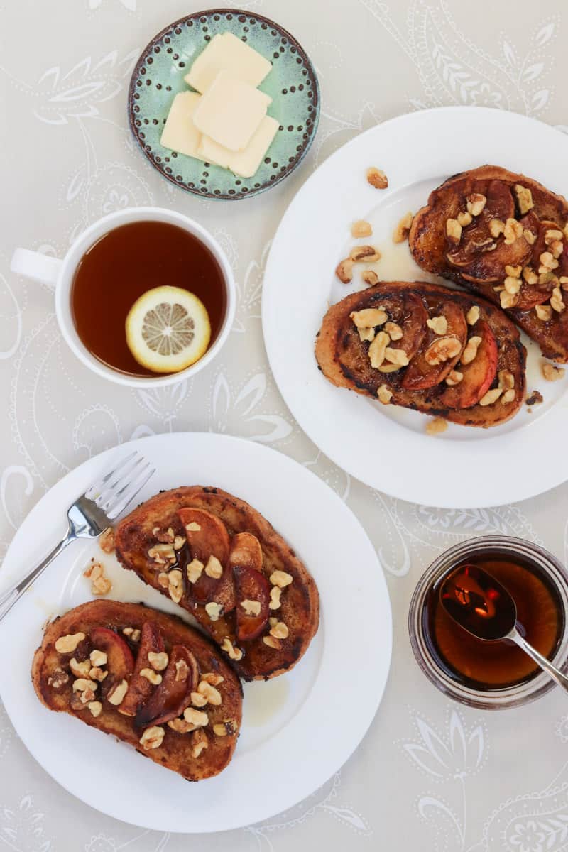 Apple Cinnamon French Toast on white plates with cup of tea, vegan butter and bowl of syrup