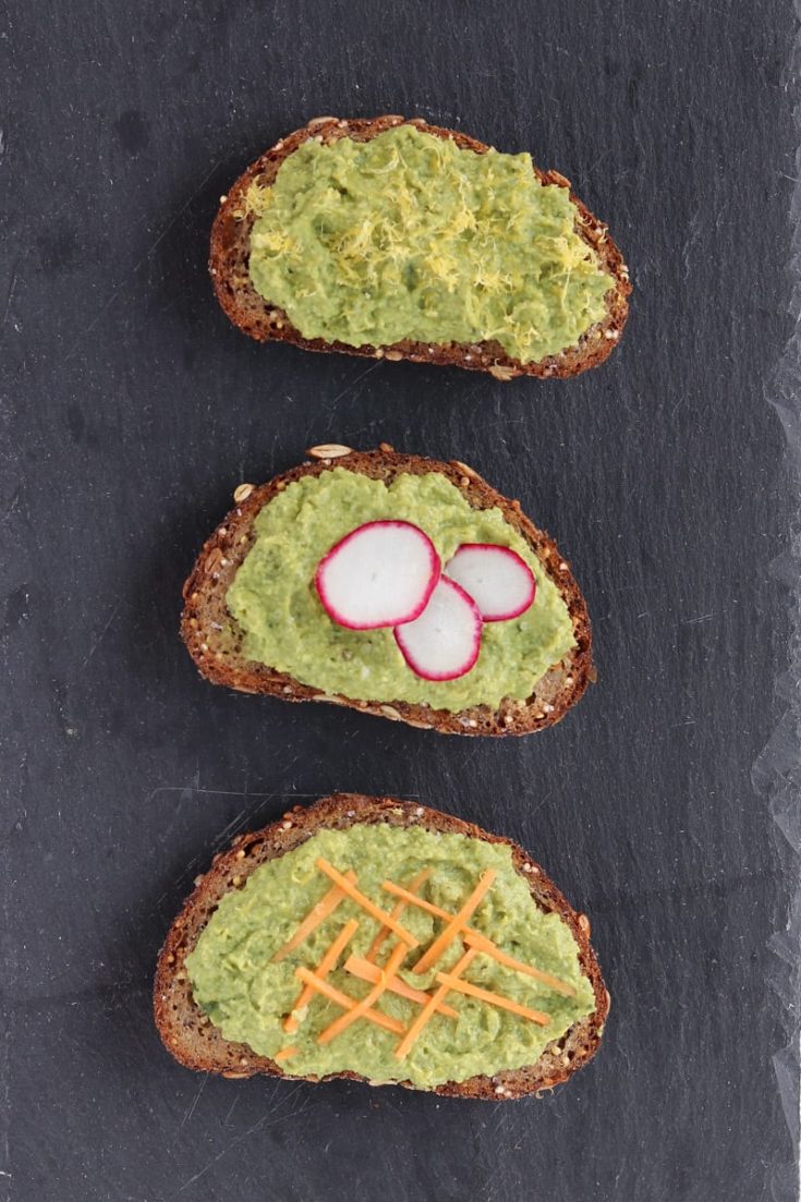 Avocado pea mash toast slices on black slate, topped with lemon zest, radish slices and slivered carrots.