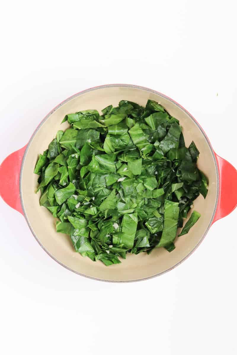 bright green collard greens and garlic in a red dutch oven.