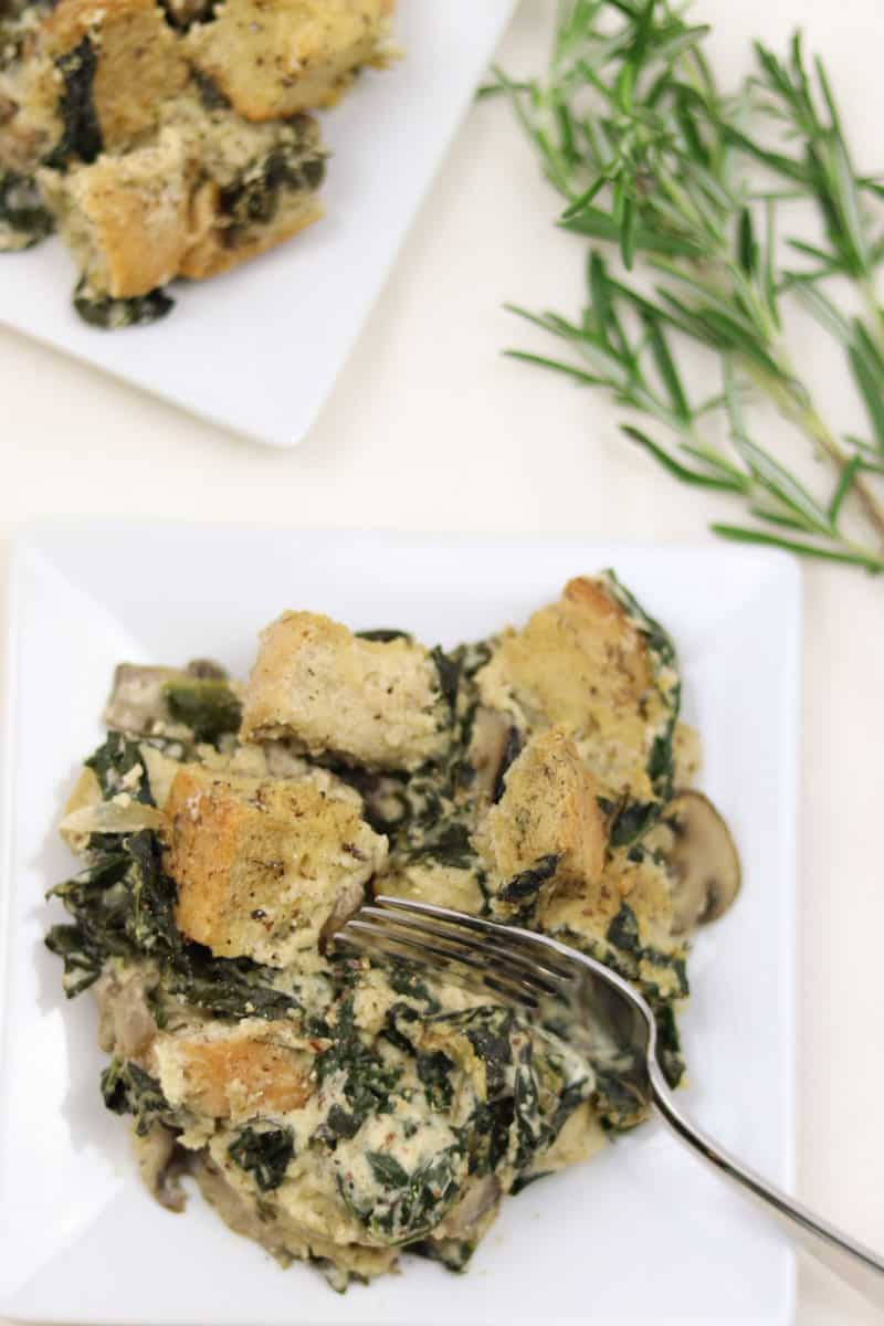 Kale Mushroom Bread Pudding in a white plate with fork and rosemary