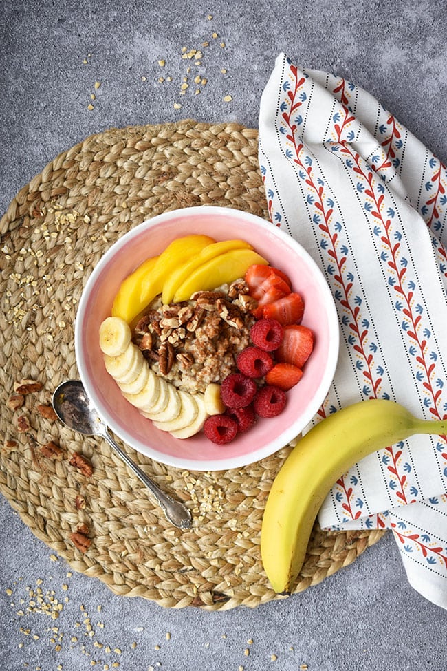 Maple pecan oatmeal topping strawberry smoothie bowl with bananas, mango and strawberries.