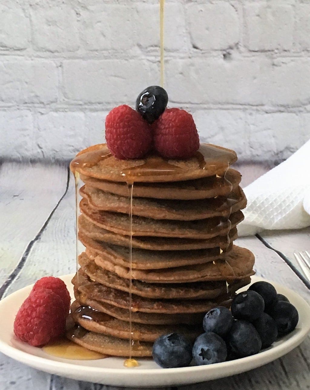 Lentil banana pancakes stacked with berries and syrup pouring over the top.