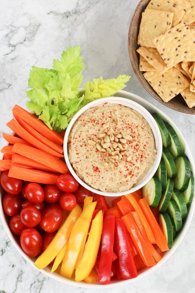 classic hummus veggie platter with carrots, cucumbers, cherry tomatoes, bell peppers celery and crackers