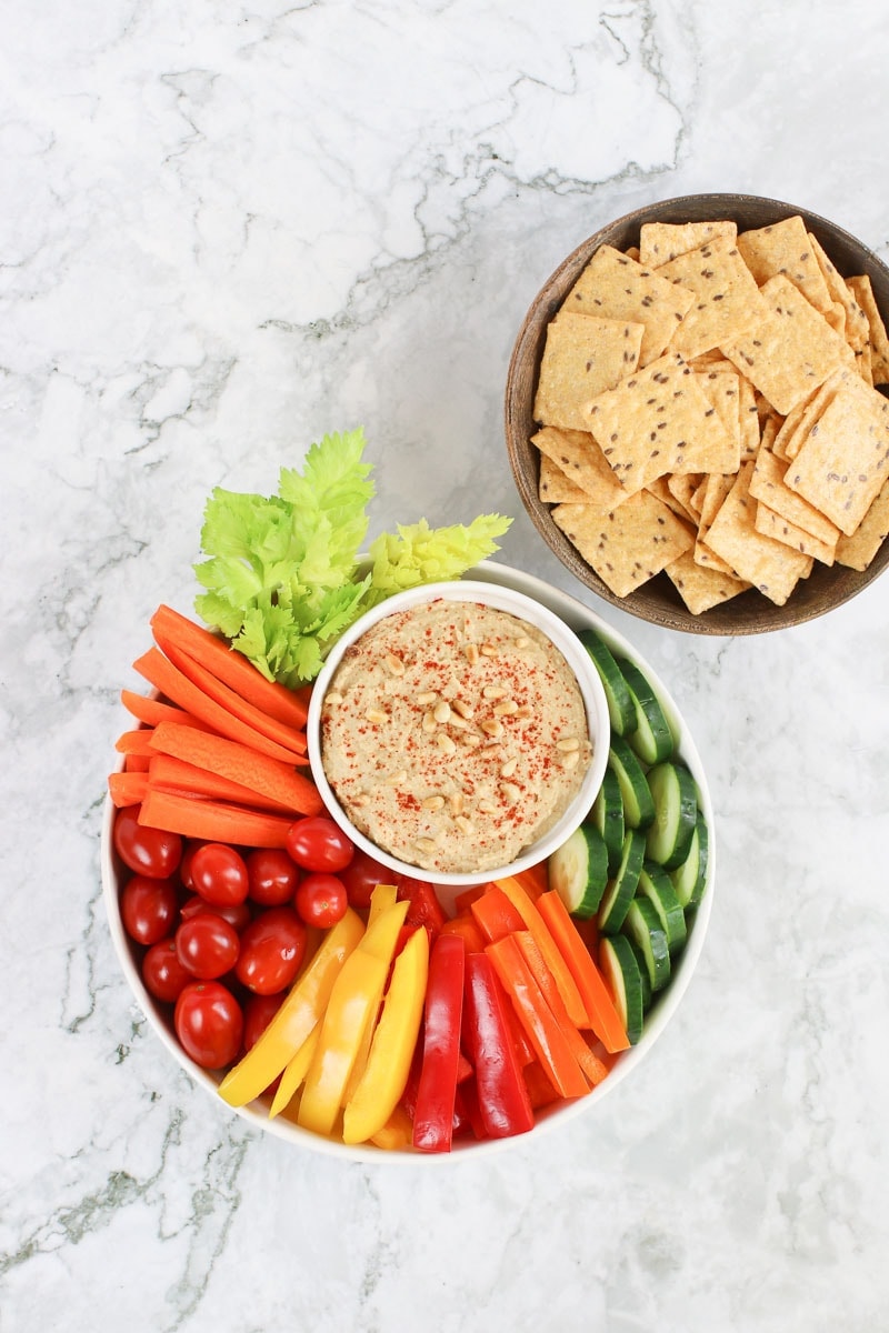 Oil free hummus on a white platter with fresh sliced veggies and rice crackers