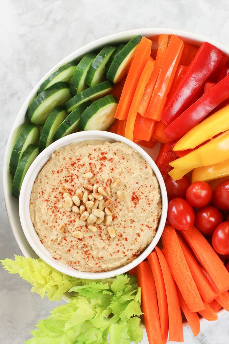 Oil free hummus on a white platter with fresh sliced veggies and rice crackers