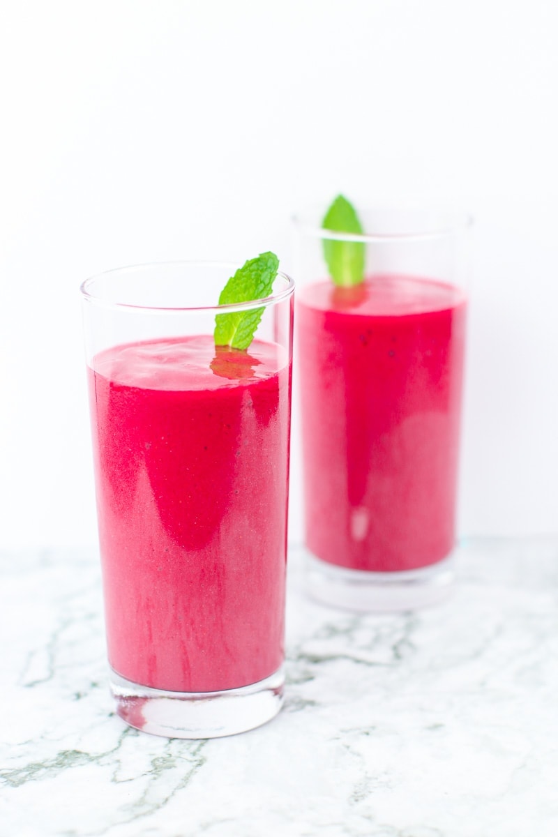 2 tall glasses of hibiscus tea pink smoothies with mint garnish