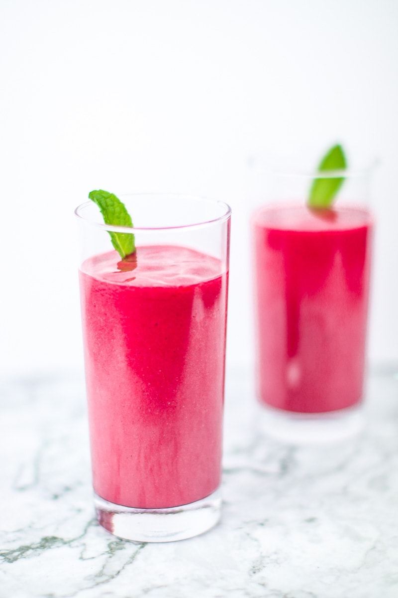 2 tall glasses of hibiscus tea pink smoothies with mint garnish