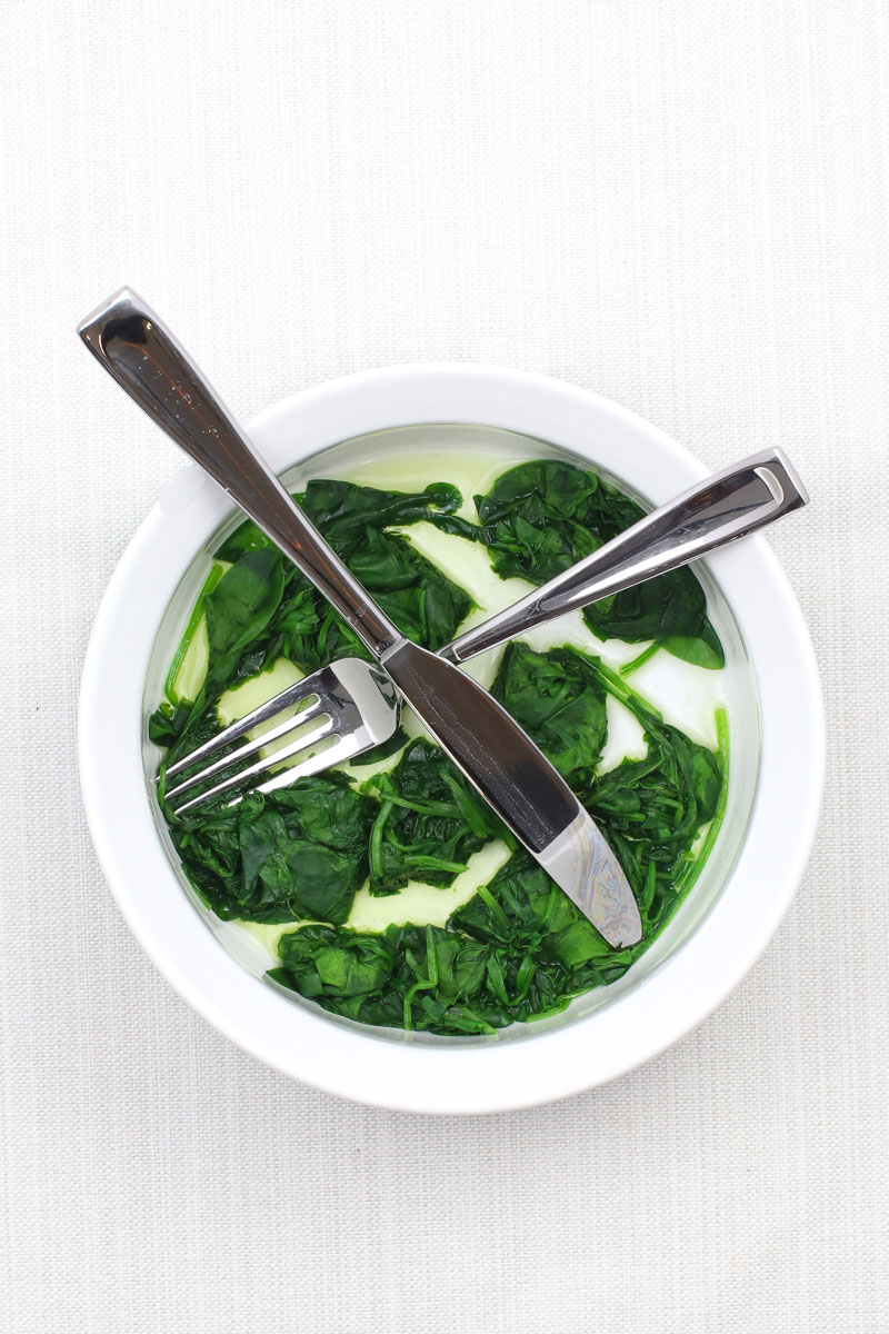 Cooked Spinach in a white bowl with a knife and fork
