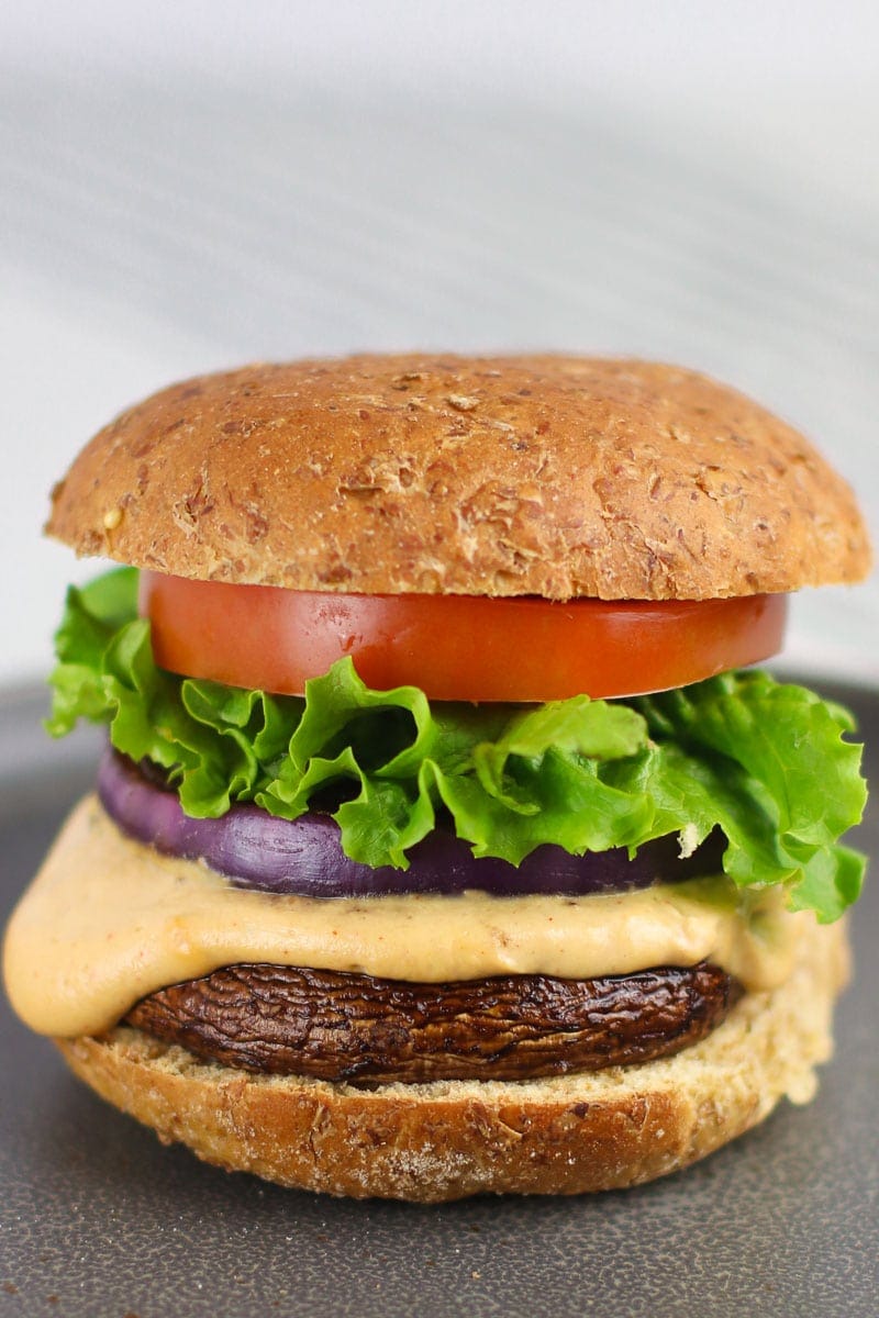 Close up of vegan portobello mushroom burger with cheddar sauce lettuce tomato and red onion