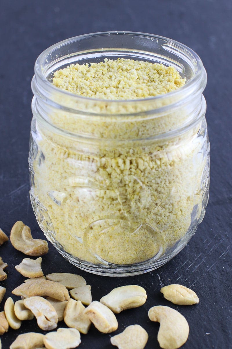 Mason jar with vegan Parm on black slate, with cashews in foreground.