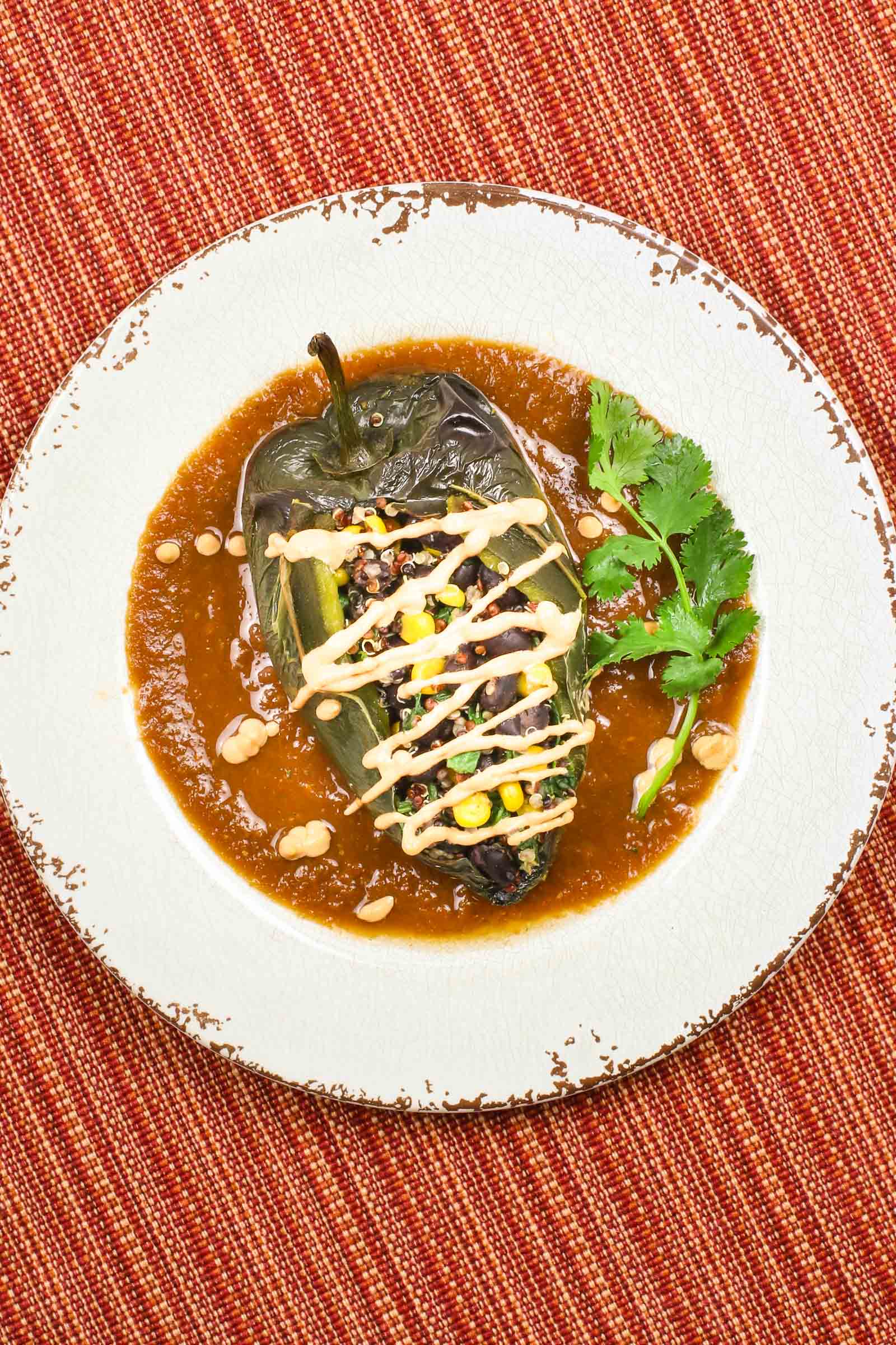 vegan chile relleno on with red sauce and vegan cheese sauce, on a red and orange placemat