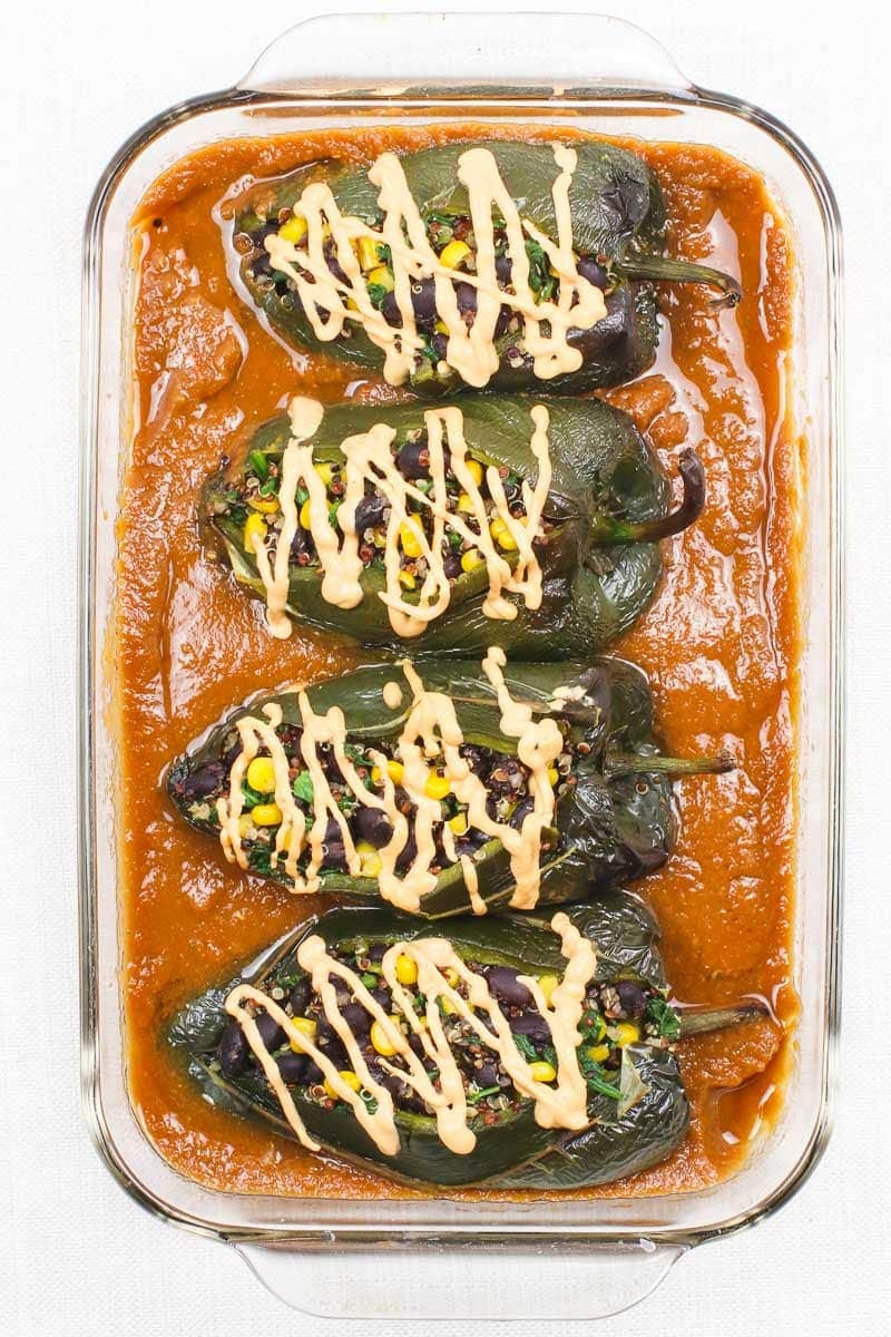 vegan chile relleno in a baking dish with red sauce and vegan cheese sauce