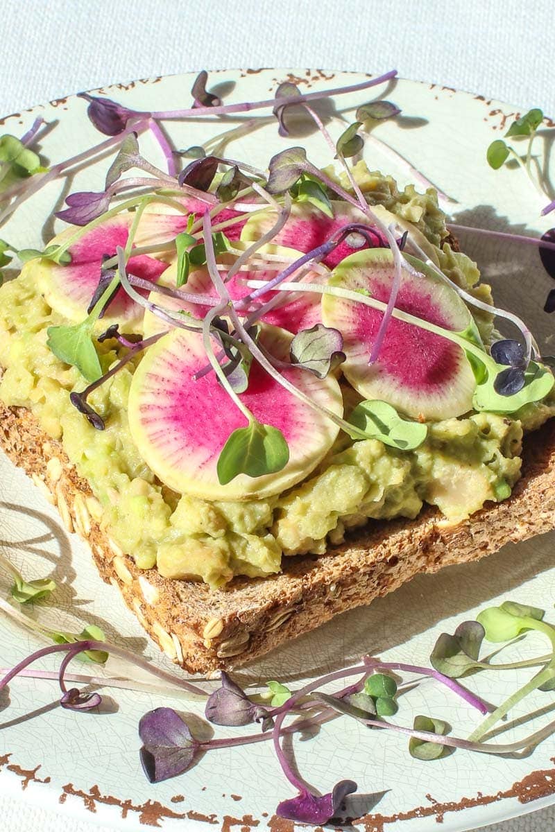 close up of vegan egg salad on toast with beauty heart radishes and micro greens on a plate