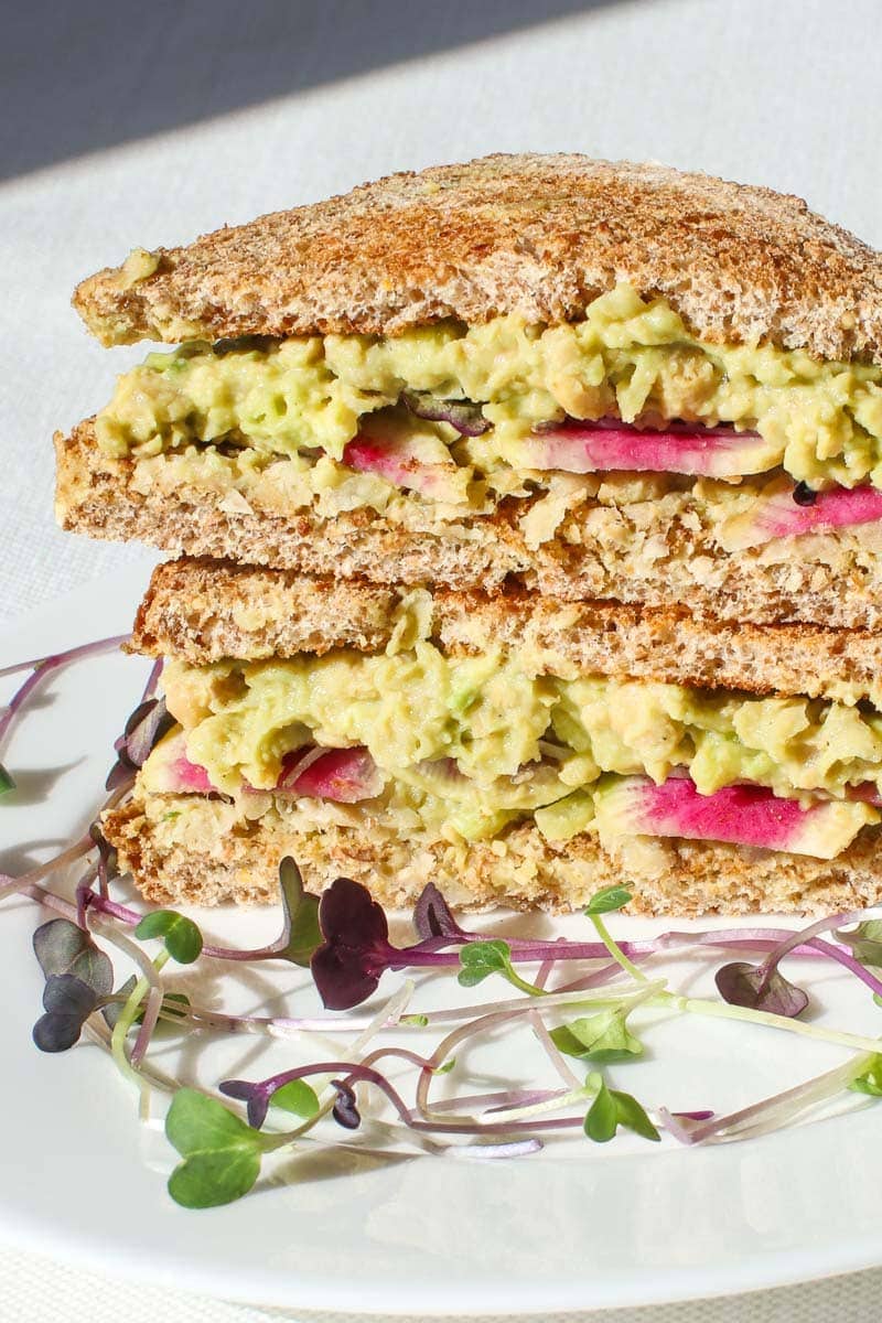 vegan egg salad sandwich on toast stacked with beauty heart radishes and micro greens on a plate