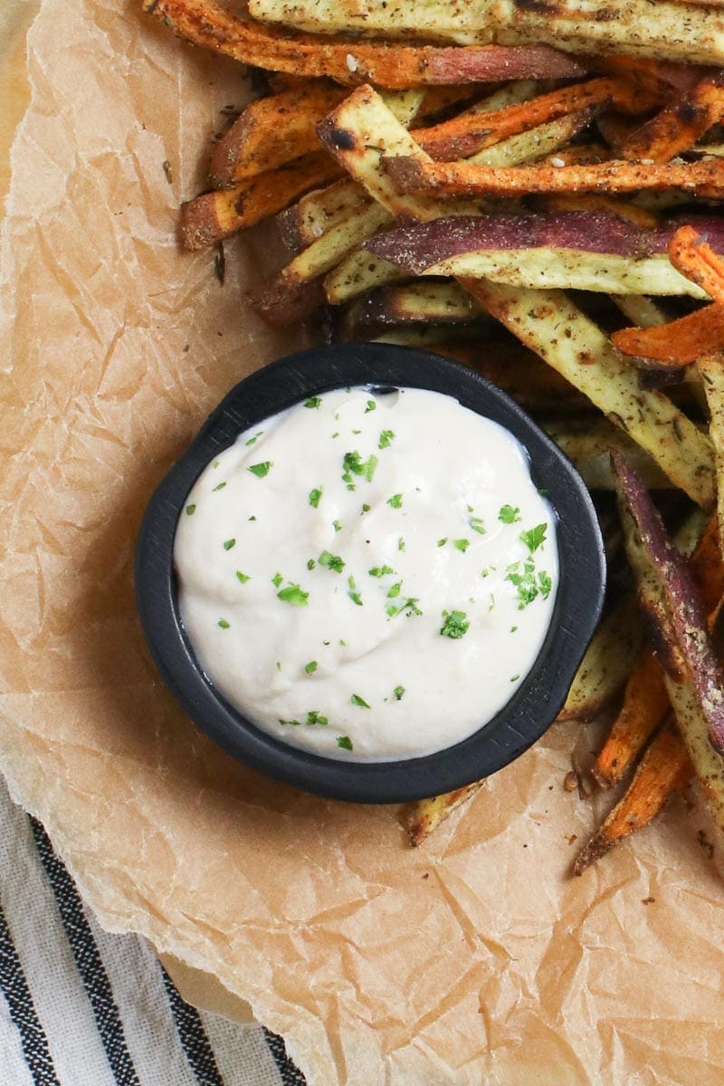 vegan oil free aioli in a black dish with baked sweet potato fries on brown parchment paper