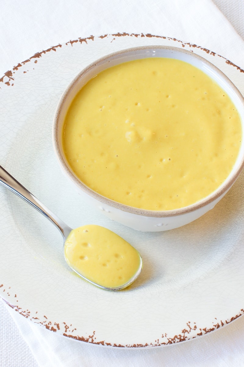 Chickpea Cheese Sauce in a white bowl on a white plate with a spoon
