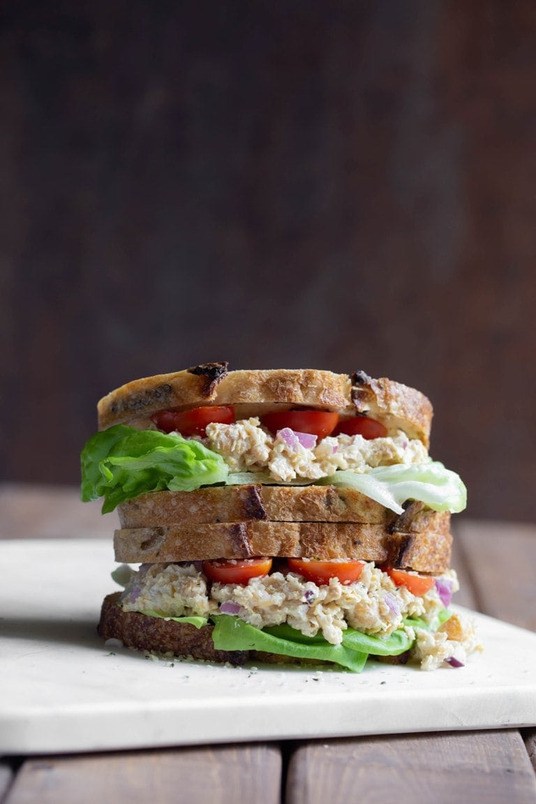 Stacked vegan Caesar Smashed Chickpea Sandwich on a white cutting board with black background