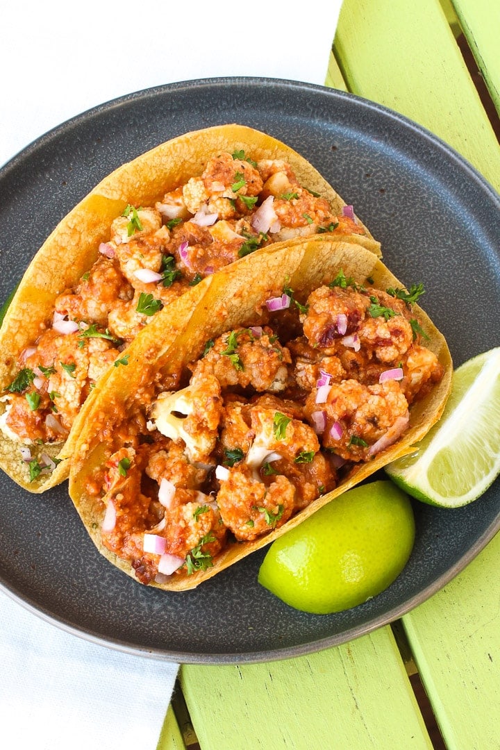 Cauliflower Tacos with Romesco Sauce close up on a dark gray plate with limes on a lime green table