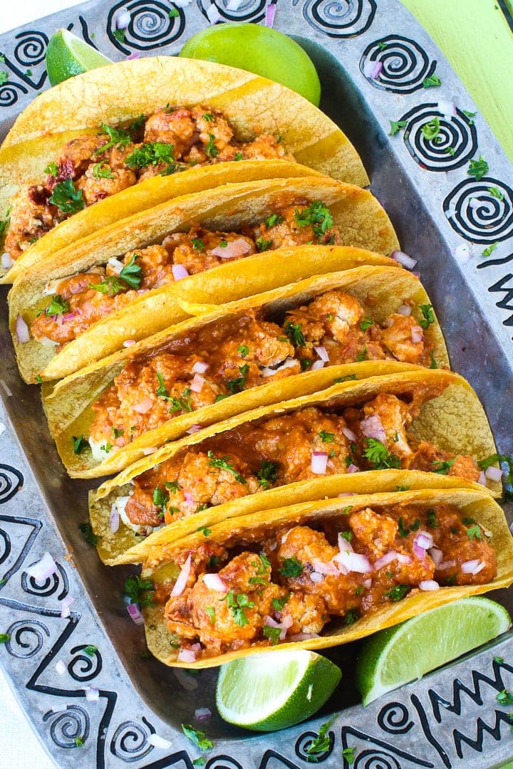 Cauliflower Tacos with Romesco Sauce on a pewter platter with limes on a lime green table