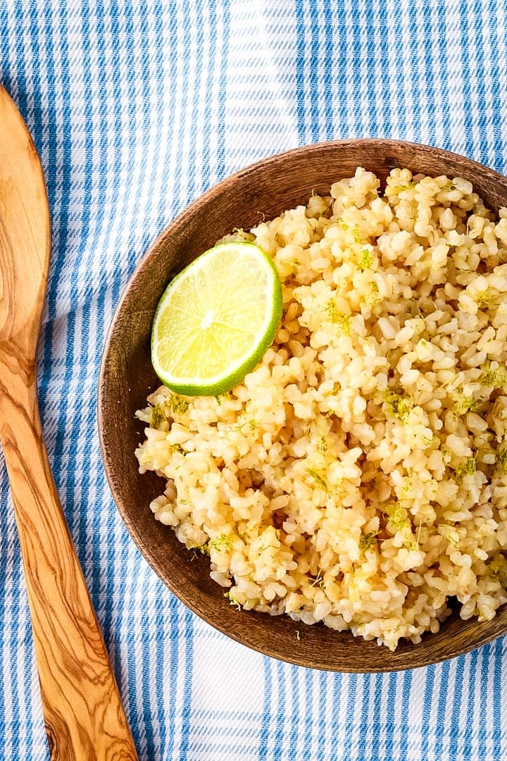 Bowl of coconut lime rice in a wooden bowl with a wooden spoon on a blue plaid towel