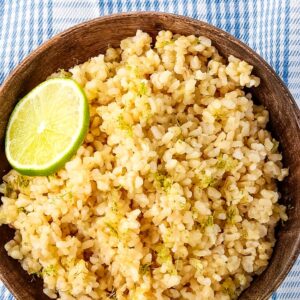 close up of Bowl of coconut lime rice in a wooden bowl with a wooden spoon on a blue plaid towel