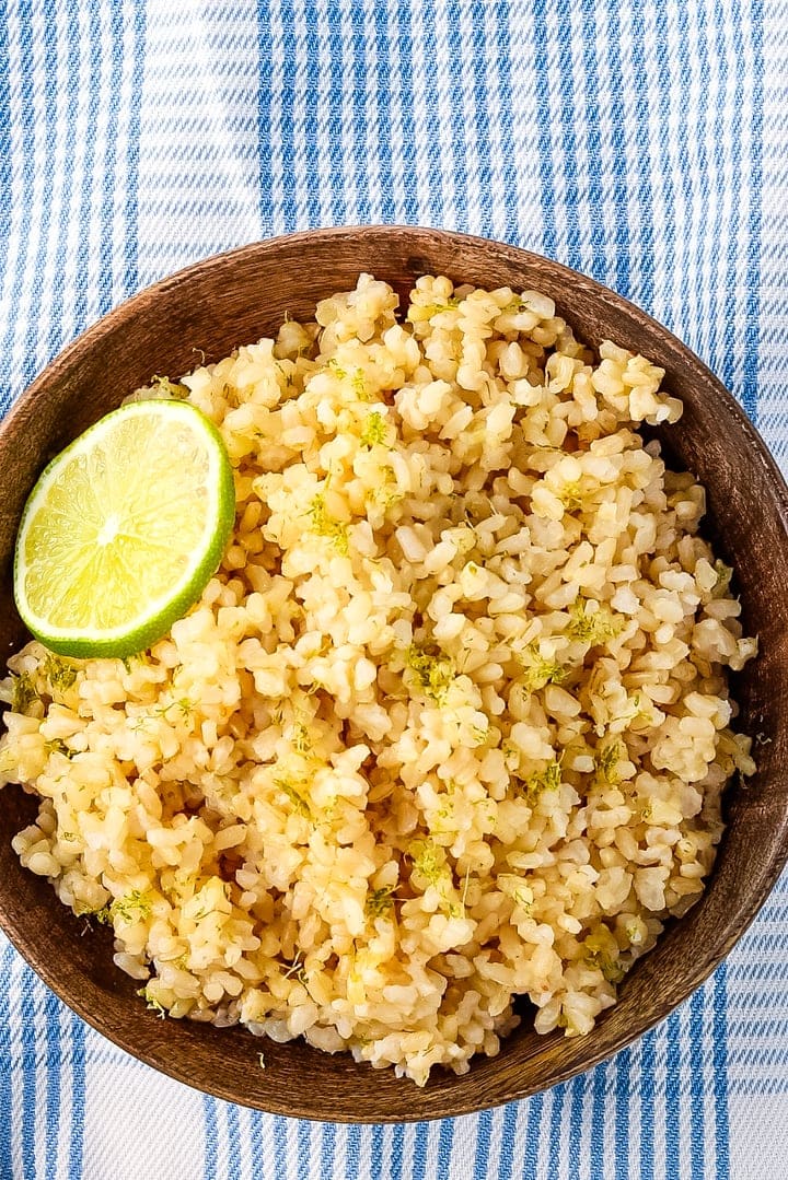 close up of Bowl of coconut lime rice in a wooden bowl with a wooden spoon on a blue plaid towel