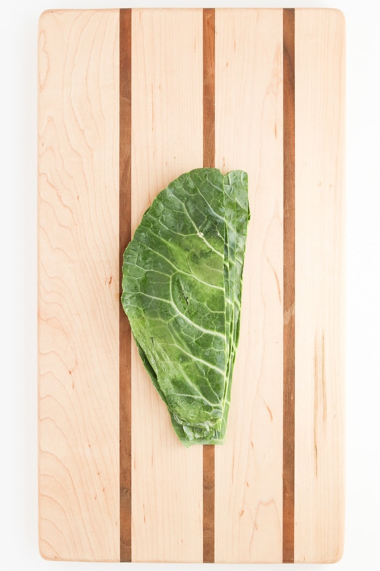 collard green leaf halves piled on top of each other on a cutting board.