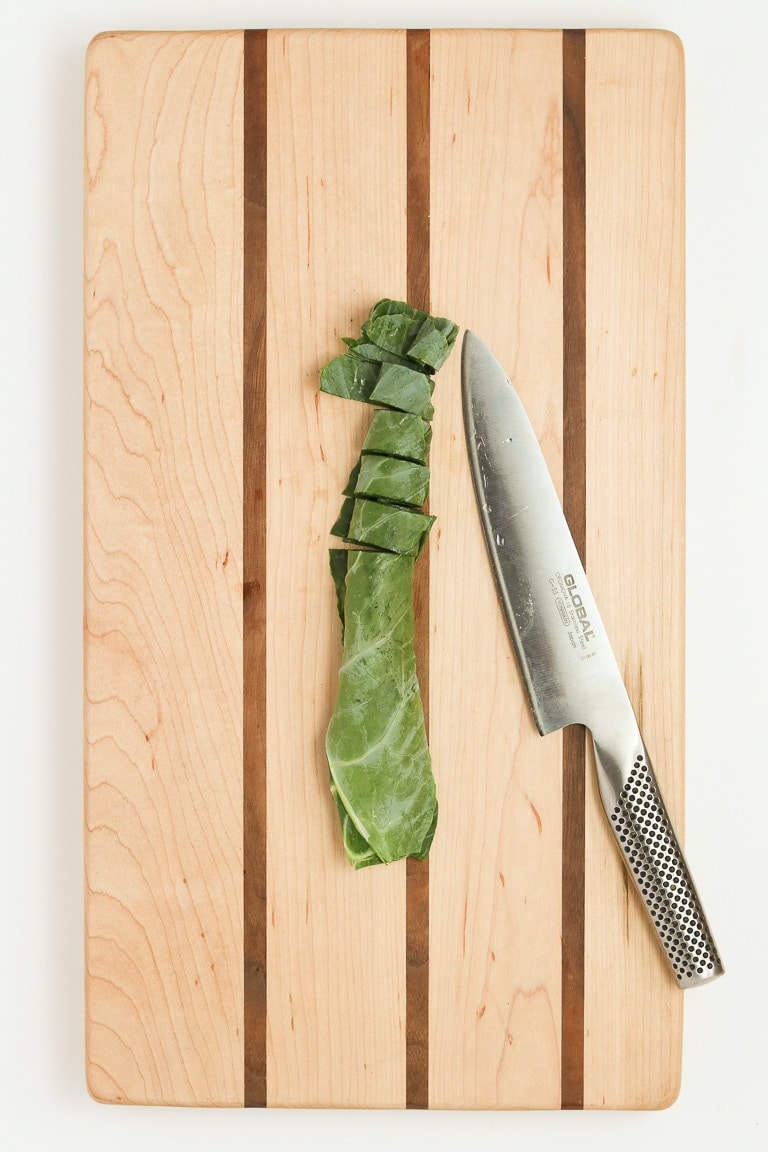 collard green leaf rolled up and cut into 1-inch pieces on a cutting board with chef's knife.
