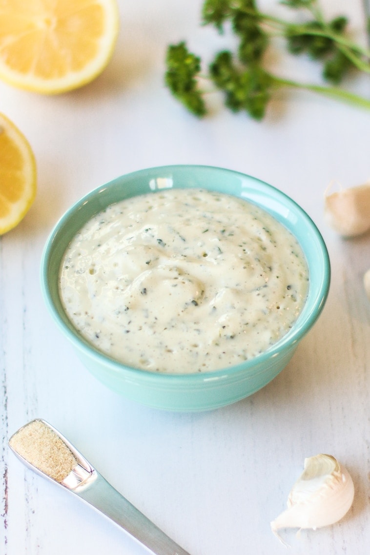close up of Oil Free Dairy Free Ranch Dressing in pale blue bowl with lemons, parsley garlic 