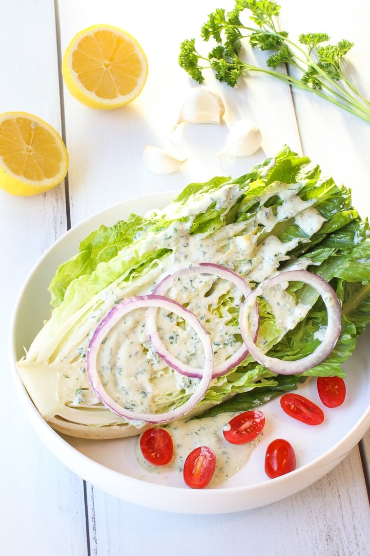 Romaine lettuce wedge with ranch dressing, red onions slices, slices cherry tomatoes, lemon, garlic and parsley