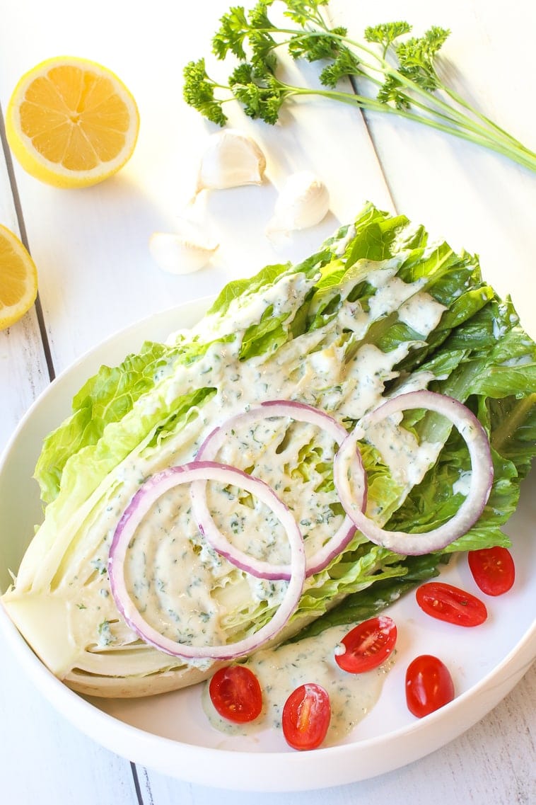 Romaine lettuce wedge with ranch dressing, red onions slices, slices cherry tomatoes, lemon, garlic and parsley