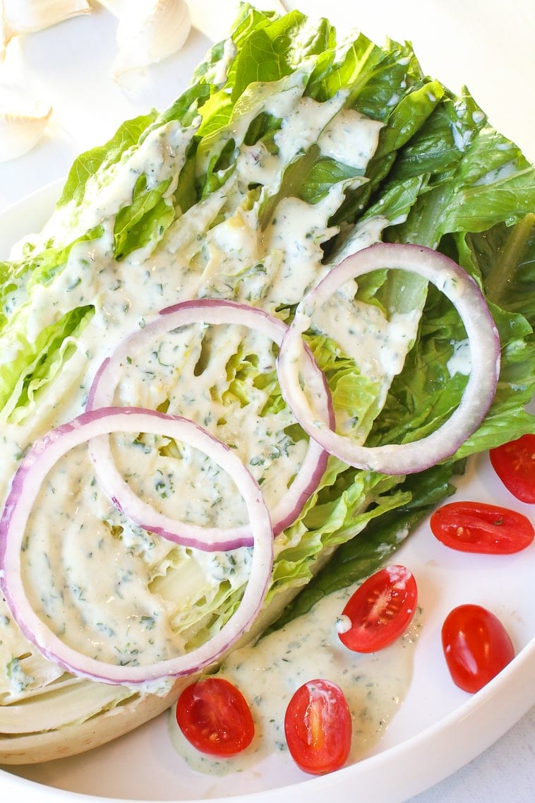 close up of Romaine lettuce wedge with ranch dressing, red onions slices, slices cherry tomatoes, lemon, garlic and parsley