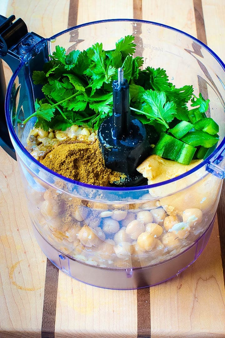 Ingredients in a food processor, cilantro, cumin, tahini, chickpeas, miso paste