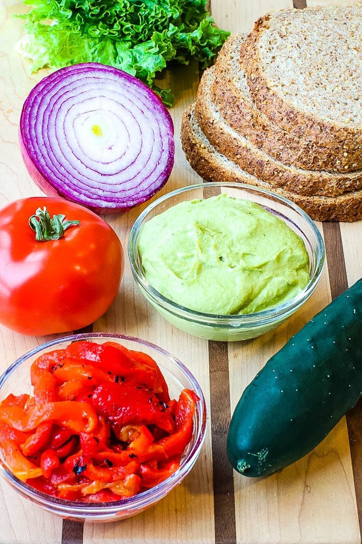 spicy hummus on a cutting board with bread, tomato, red onion, red peppers, cucumber and lettuce