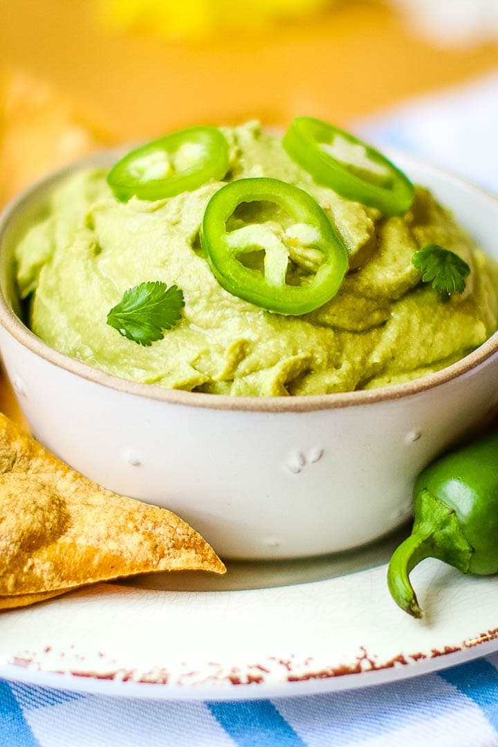 Close up of Spicy oil free hummus in a bowl with tortilla chips and jalapeño on a blur plaid towel with daisies