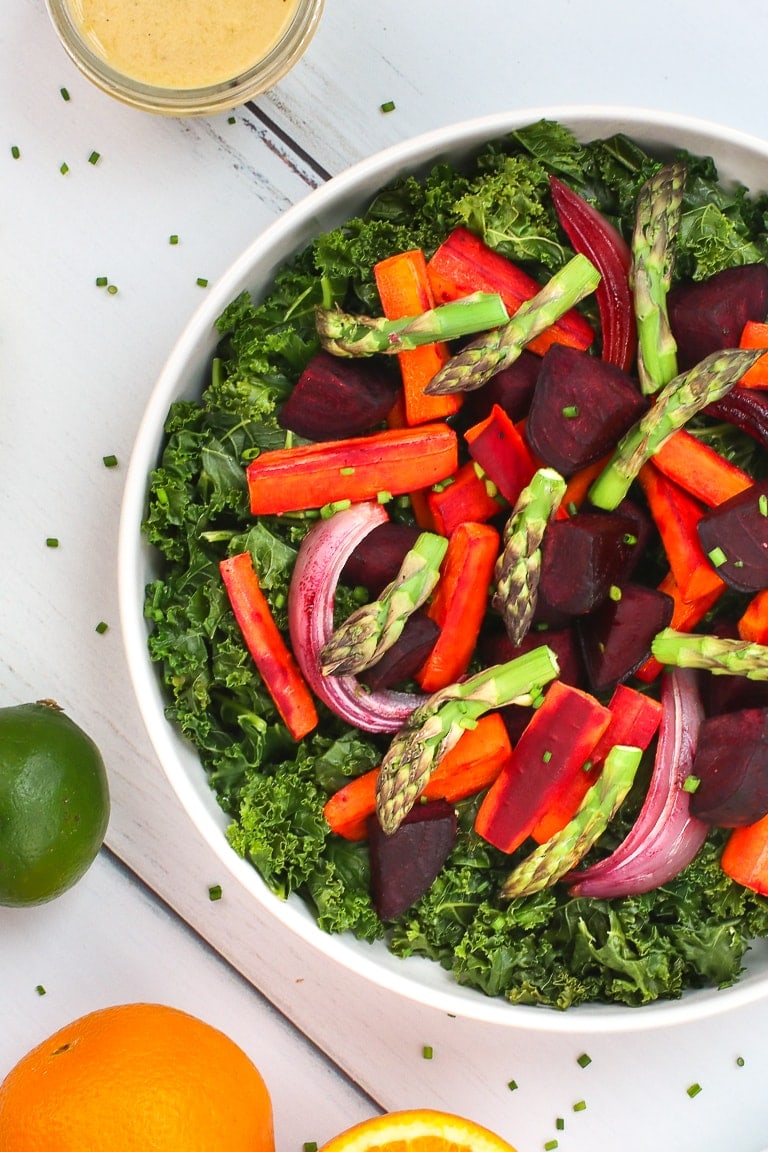 Warm kale salad with roasted carrots, beets and asparagus and citrus dressing on a white table with lemons, oranges and lime