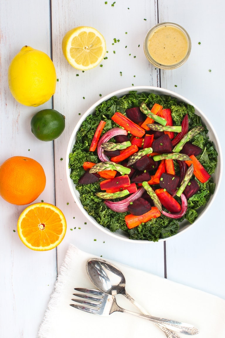 Warm kale salad with roasted carrots, beets and asparagus and citrus dressing on a white table with lemons, oranges and lime