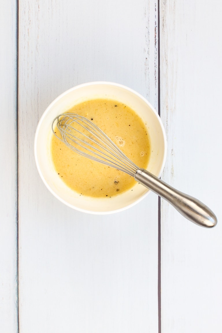 citrus dressing in a white bowl with whisk on a white board table