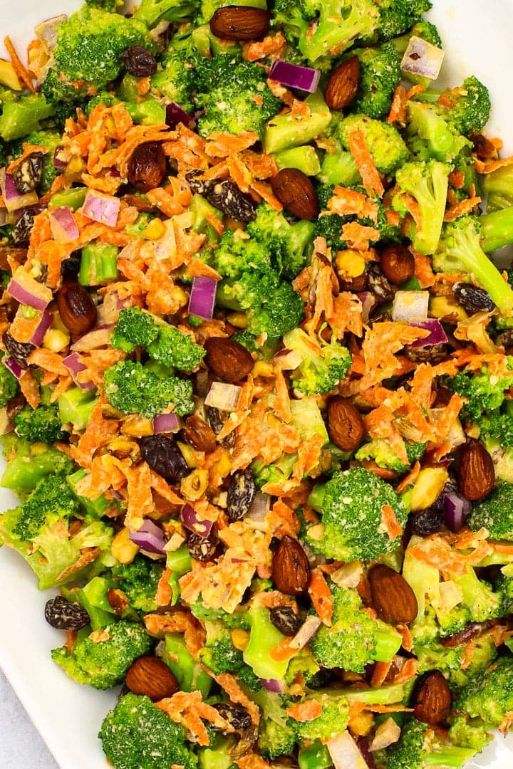 close up of vegan broccoli salad with shredded carrots, diced red onion, raisins, smoky almonds and sweet & creamy dressing.