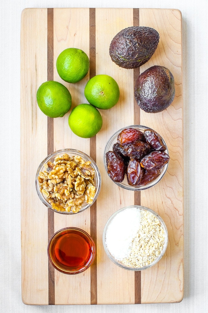 vegan key lime pie mini tarts ingredients on a cutting board: avocados, limes, walnuts, maple syrup, dates, oats, shredded coconut.