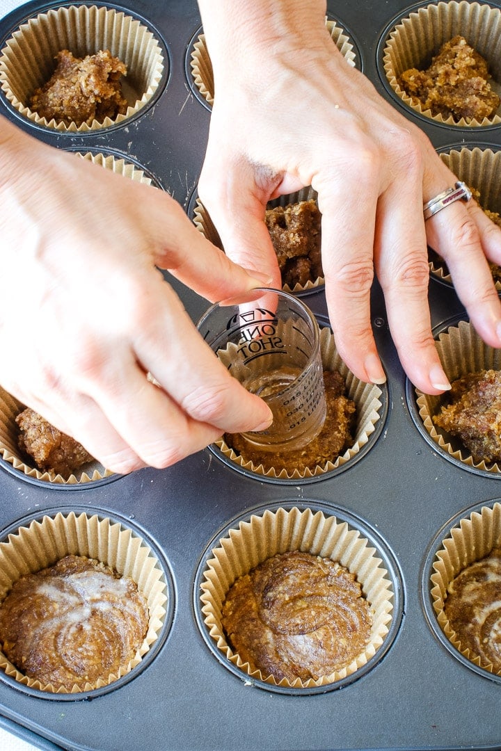 hand pressing crust into baking cups in a muffin pan using a shot glass.