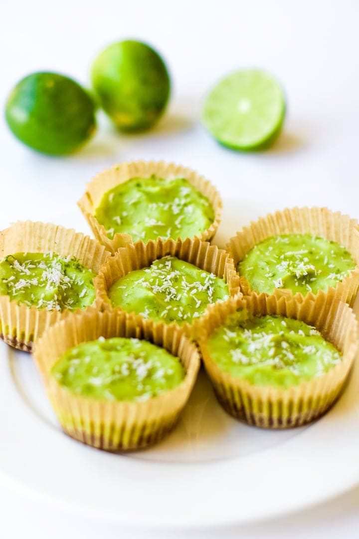 white plate with vegan key lime pie mini tarts in baking cups with limes in background.