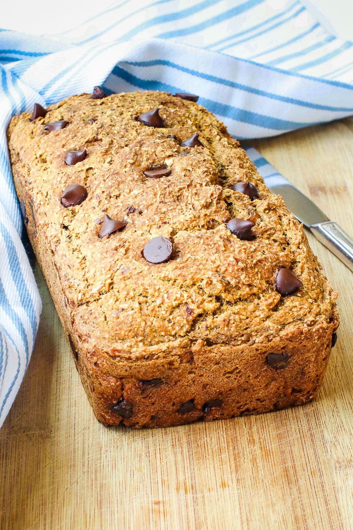  pumpkin bread with chocolate chips on a cutting board with a a pale blue striped towel and a knife