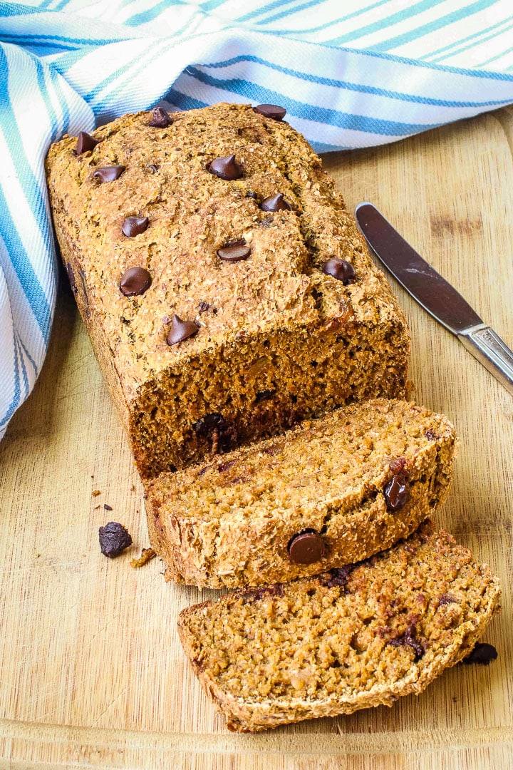 sliced pumpkin bread with chocolate chips on a cutting board with a a pale blue striped towel with a knife