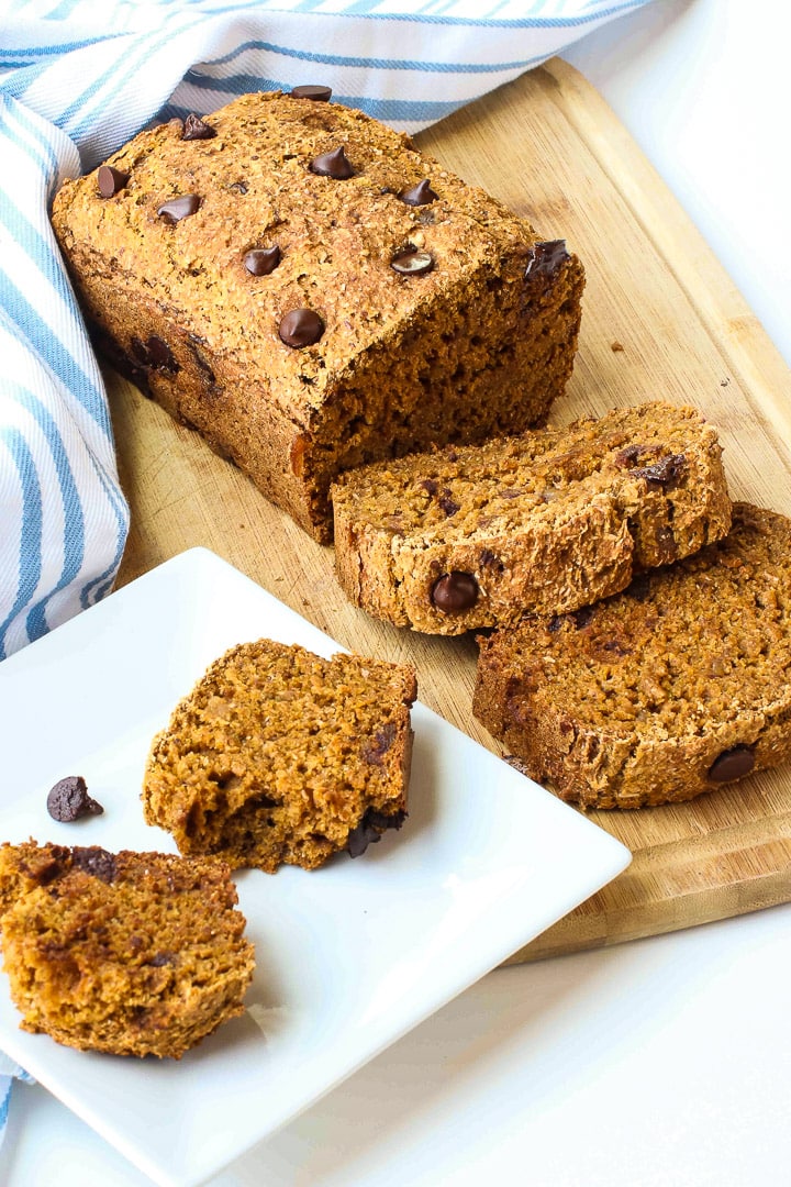 sliced pumpkin bread with chocolate chips on a cutting board with a a pale blue striped towel and a white plate with a piece of bread