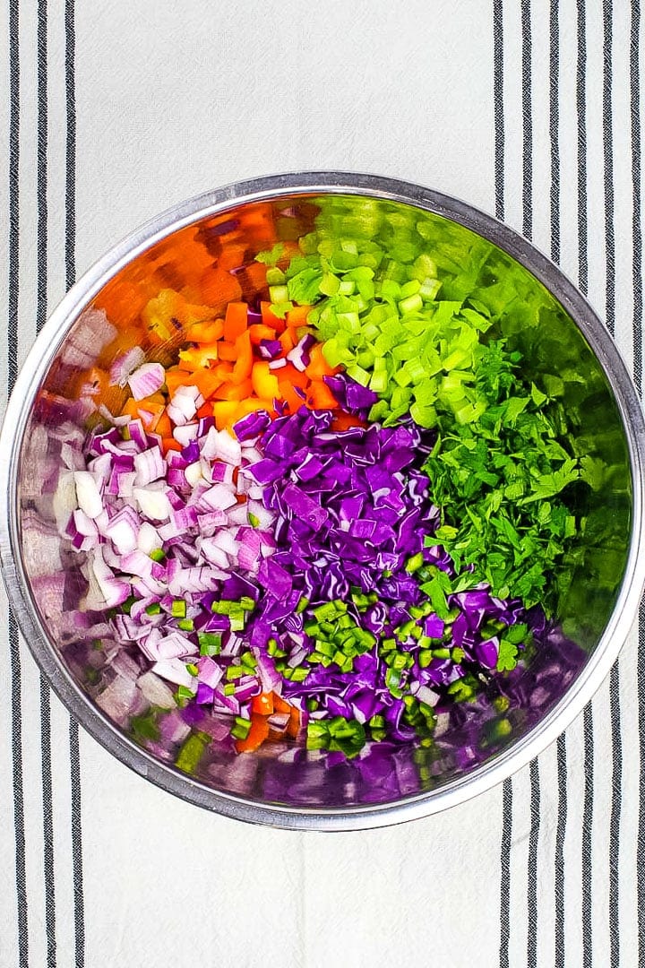 chopped chickpea salad veggies in a stainless steal bowl on striped towel.