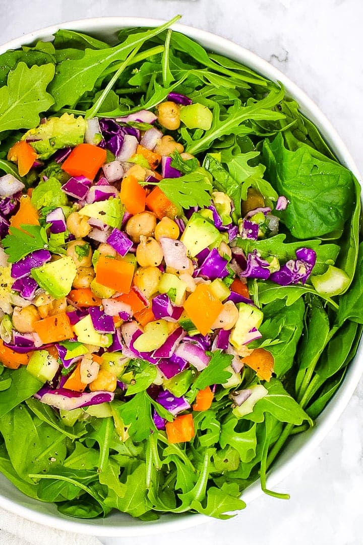 simple chickpea salad on a bed of arugula and spinach in a wide white bowl on marble