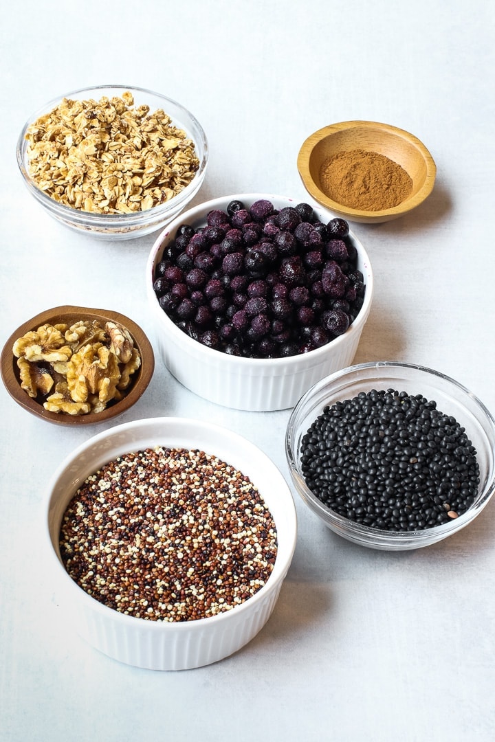 small bowls on a gray background with frozen blueberries, tricolored quinoa, walnuts, black lentils, cinnamon and granola