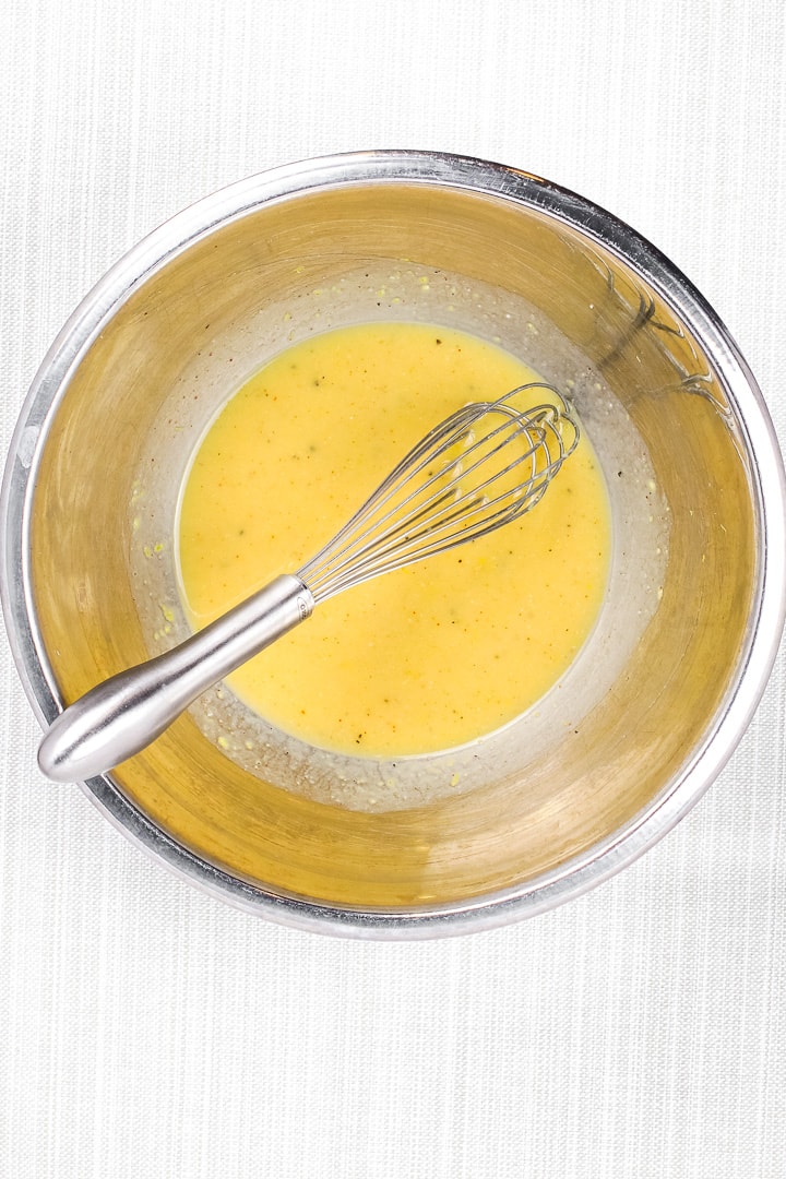 Yellow lemon, dijon mustard and aquafaba dressing in a stainless steel bowl with whisk